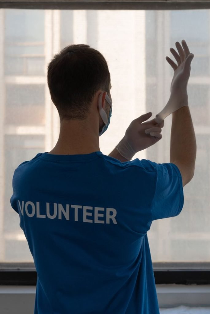 a-man-wearing-surgical-gloves-7473990 A volunteer wearing gloves ready to assist in a safe, indoor setting.