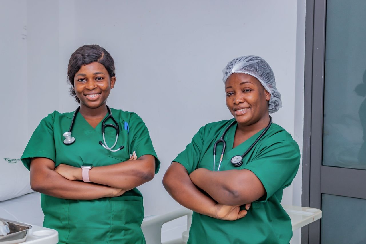 gallery-04 Two female nurses in green scrubs smiling confidently in a hospital room. Professional healthcare workers.
